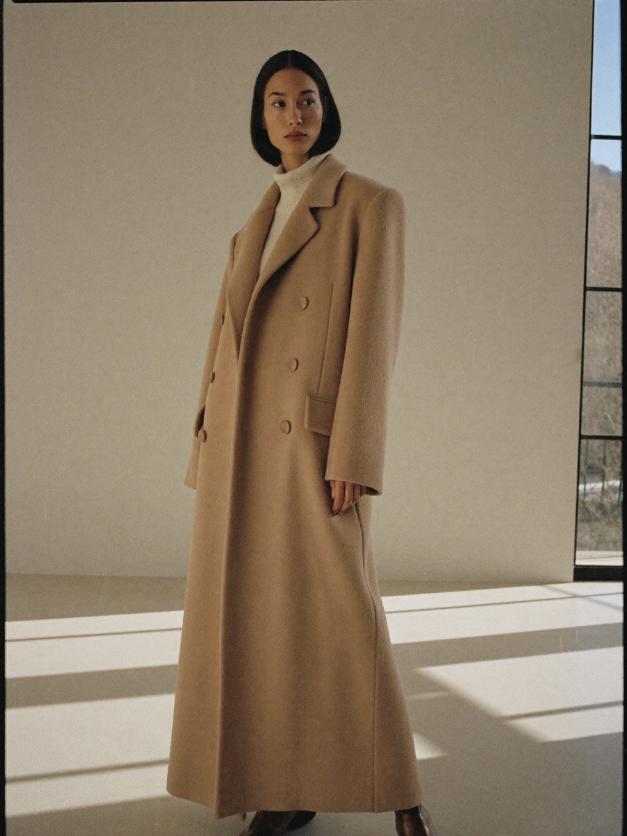 A woman in a camel cashmere coat standing in a sunlit gallery
